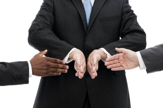 Businessman avoiding handshake between african descent and caucasian businessmen (Getty Images)